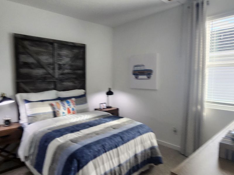 A cozy bedroom with striped bedding, rustic headboard, and understated decor. Bright window and modern lamps complete the look.