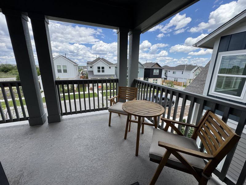 A charming balcony with wooden furniture and neighborhood views under a vast blue sky.