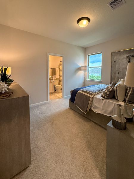 A cozy bedroom features soft carpeting, a large bed, and an en-suite bathroom illuminated by warm, stylish lighting.