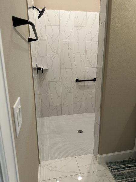A modern shower with marble wall tiles, sleek black fixtures, and a textured floor offering a sophisticated touch. A modern shower with marble wall tiles, sleek black fixtures, and a textured floor offering a sophisticated touch.