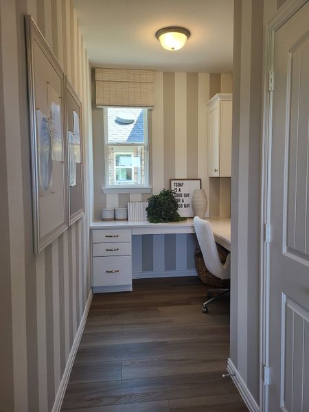 A cozy home office with striped walls, a built-in desk, stylish decor, and warm wood flooring.