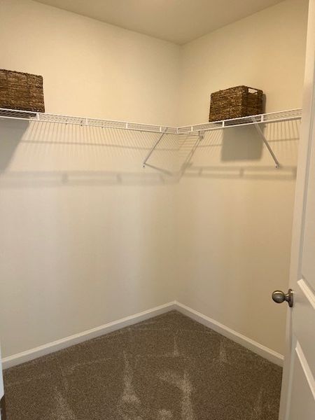 A spacious walk-in closet with wire shelving and carpeted flooring, featuring organized wicker storage baskets.