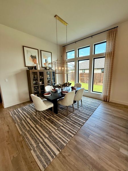 A spacious dining room with a sleek black table, elegant white chairs, and large windows offering abundant natural light.