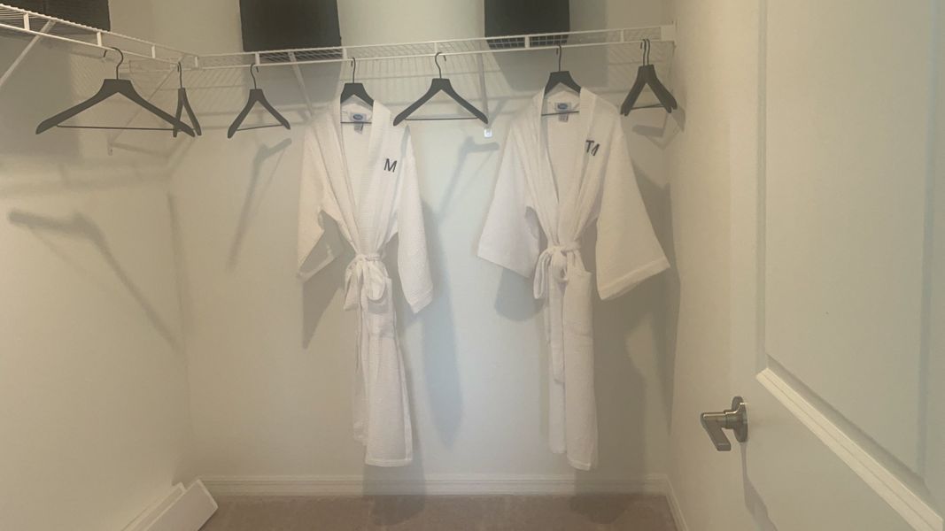 A spacious walk-in closet featuring white robes, hanging space, and sleek design accents.