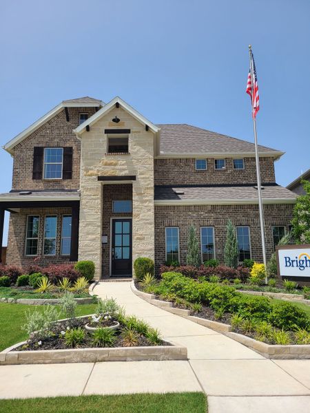 A beautiful brick and stone home with manicured landscaping in The Oaks by Brightland Homes (Red Oak, TX).
