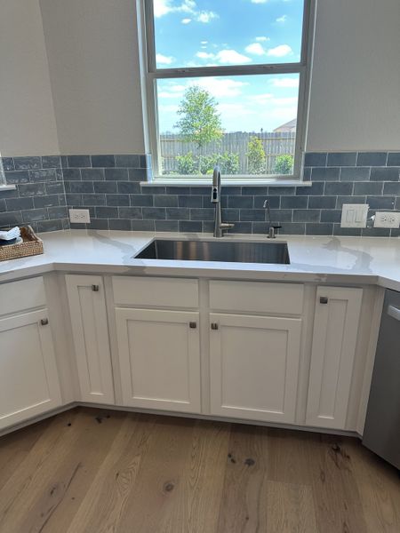 A modern kitchen with sleek white cabinets, hardwood floors, and a large window overlooking a sunny backyard.