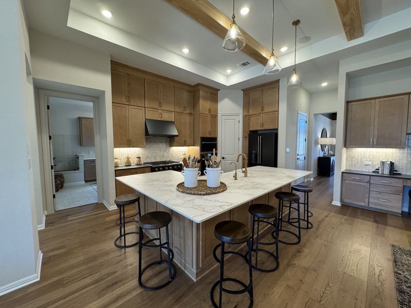A modern kitchen featuring a large marble island, wood cabinetry, and stylish pendant lighting.