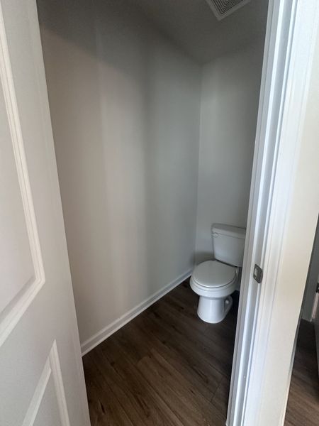 A compact bathroom with wood-style flooring and neutral walls, featuring a sleek white toilet for a minimalist design.