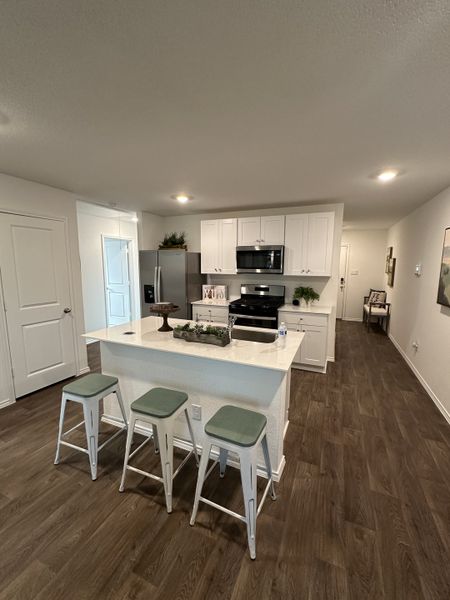 A modern kitchen with white cabinetry, a central island with bar stools, and wood-style flooring.