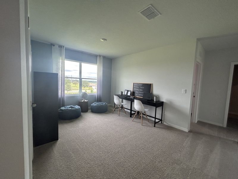 A bright study room with a modern desk, two chairs, and natural light streaming through a large window.
