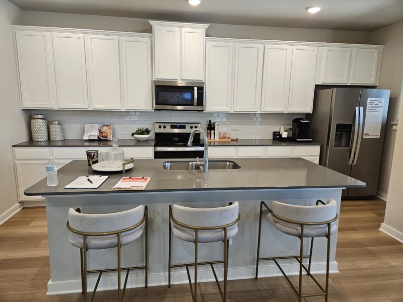 A modern kitchen with sleek gray countertops, white cabinetry, and stainless steel appliances, highlighted by stylish bar stools. A modern kitchen with sleek gray countertops, white cabinetry, and stainless steel appliances, highlighted by stylish bar stools.