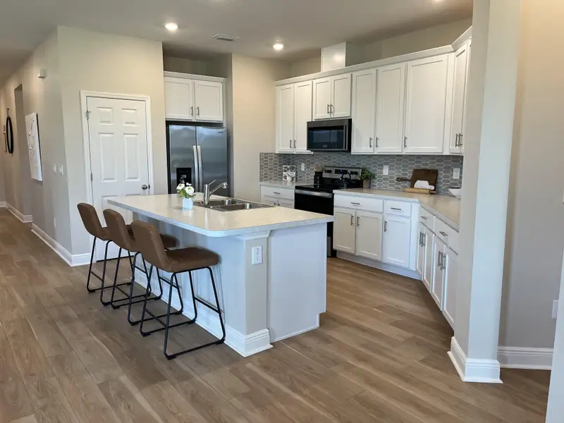 A modern kitchen with sleek white cabinets, a spacious island, and stylish seating, complemented by a chic tile backsplash.