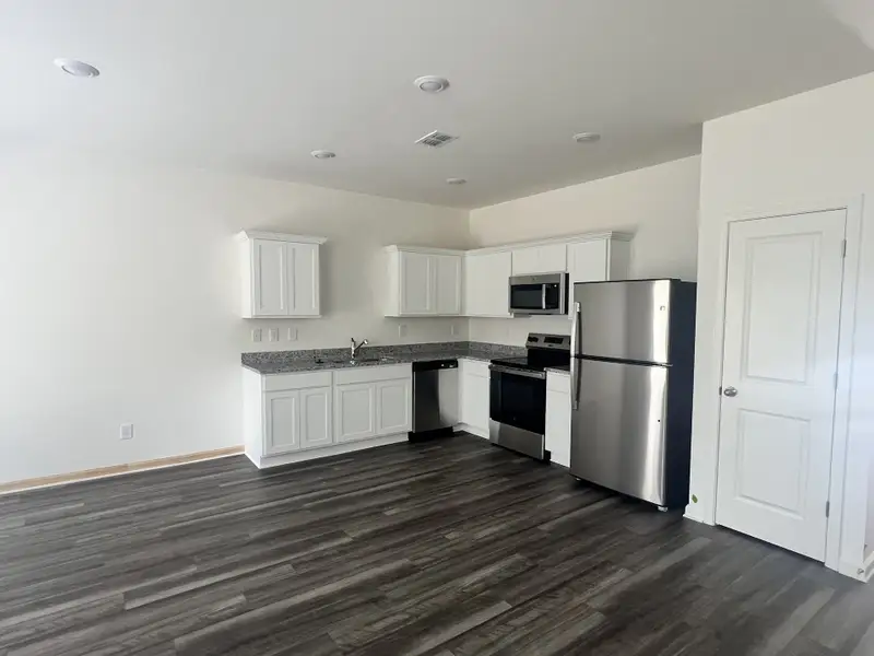 Modern kitchen with sleek stainless steel appliances, white cabinetry, and dark wood flooring.