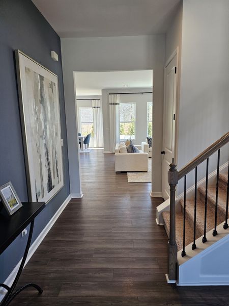 A modern hallway featuring sleek wood flooring, elegant artwork, and a cozy living area bathed in natural light.