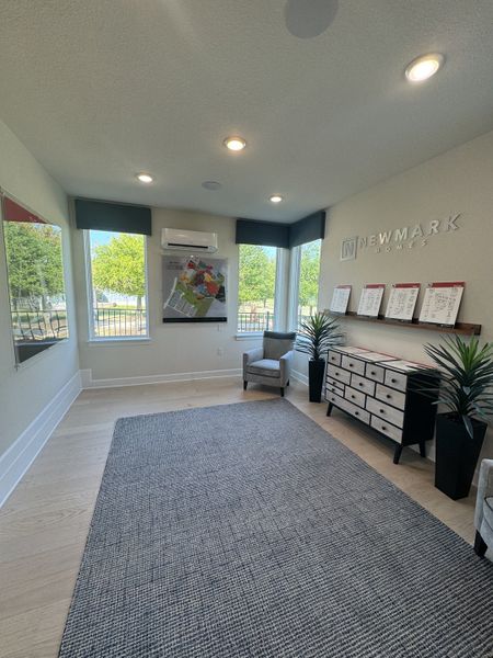 A bright, modern office with large windows, a sleek rug, a stylish dresser, and comfortable seating.