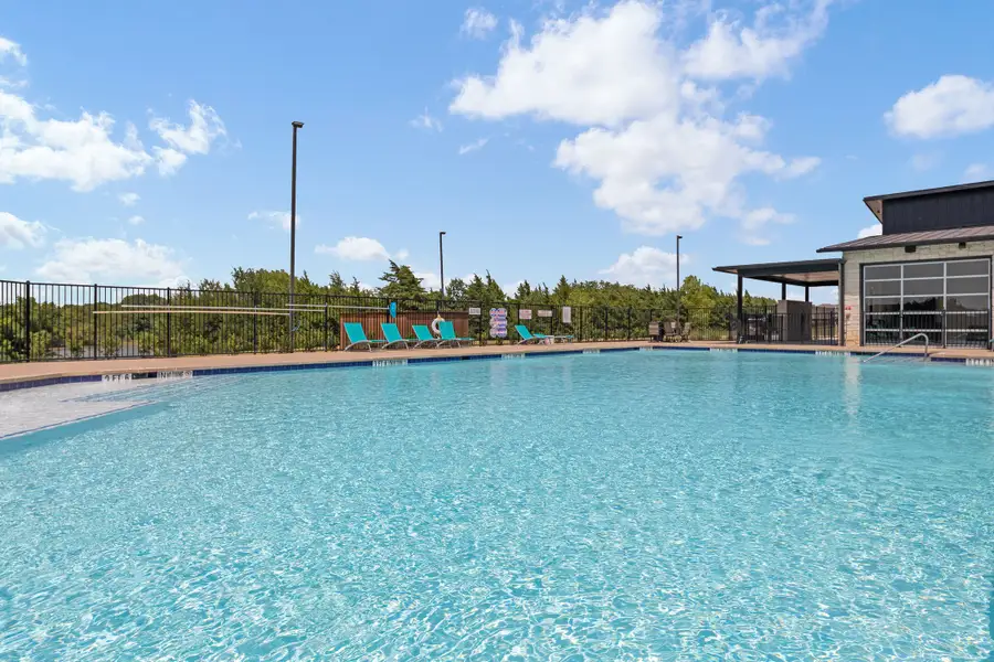 Community swimming pool with lounge chairs, iron fence, and covered clubhouse building nearby