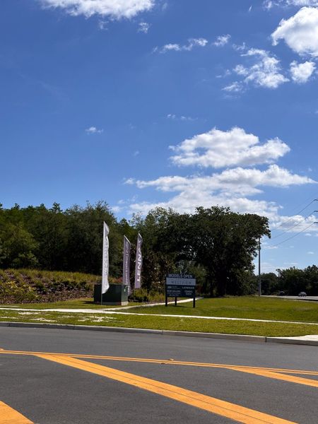 Discover Westview: Overlook Townhomes by Lennar in Kissimmee, FL. Scenic entrance with signage and flags under a blue sky.
