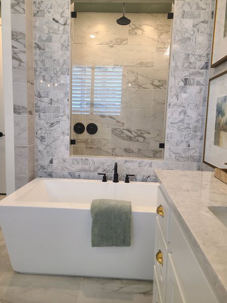 A luxurious bathroom with a sleek freestanding tub, marble walls, chic fixtures, and elegant cabinetry. A luxurious bathroom with a sleek freestanding tub, marble walls, chic fixtures, and elegant cabinetry.