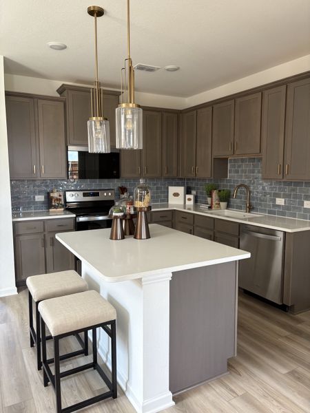 A modern kitchen featuring dark cabinets, pendant lighting, and a white island with seating.