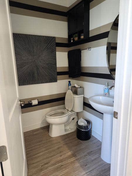 A modern bathroom with striped walls, sleek fixtures, and wood-look flooring.