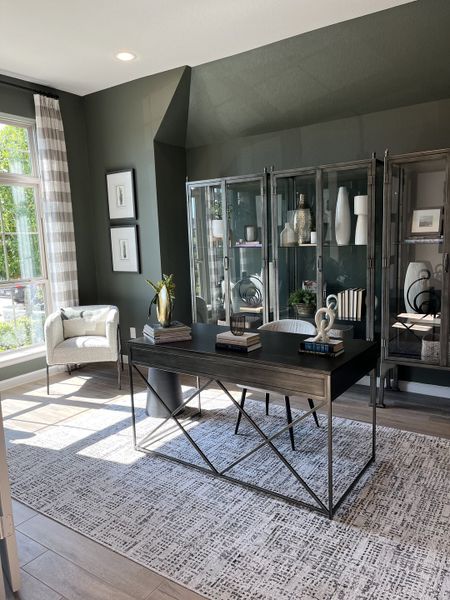 A modern office with sleek furniture, glass cabinets, and elegant decor, featuring abundant natural light and a textured rug. A modern office with sleek furniture, glass cabinets, and elegant decor, featuring abundant natural light and a textured rug.