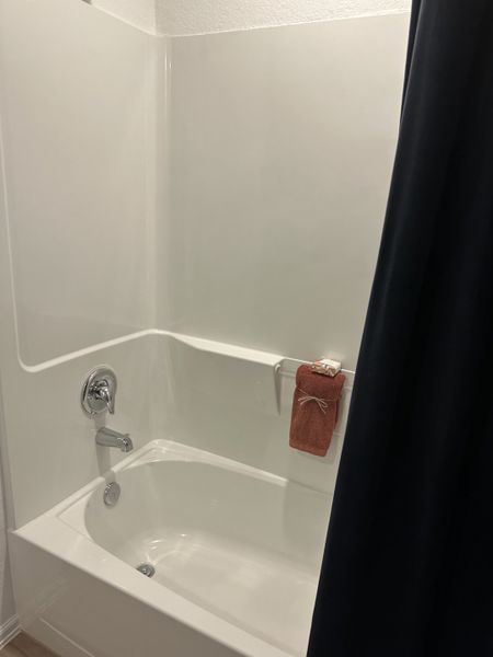 A sleek bathroom features a modern bathtub with chrome fixtures, complemented by a dark curtain and neatly folded towel. A sleek bathroom features a modern bathtub with chrome fixtures, complemented by a dark curtain and neatly folded towel.