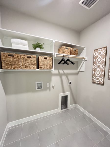 A modern laundry room with sleek gray tiles, open shelving, and woven storage baskets.