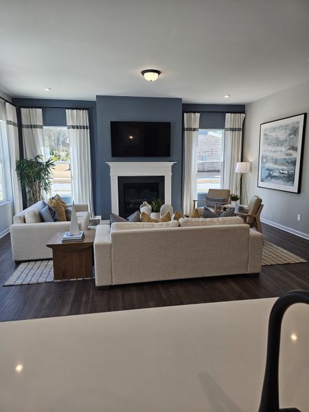 A cozy living room featuring a plush beige sectional, fireplace, and large windows with elegant drapery.