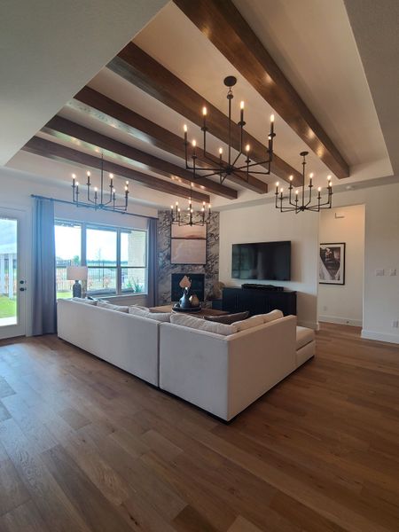 A modern living room featuring exposed beams, elegant chandeliers, a plush sectional, and large windows for natural light.