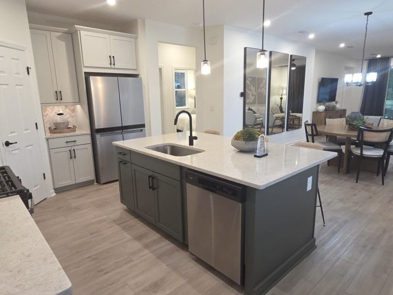 A modern kitchen with a sleek island, chic lighting, stainless steel appliances, and an elegant dining area.