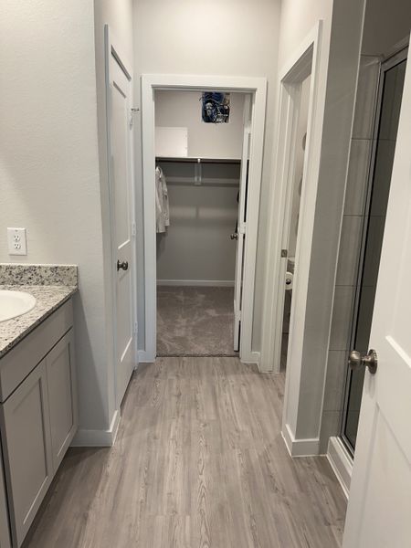 A modern hallway with sleek laminate flooring and a walk-in closet, adjacent to a stylish bathroom with a granite countertop.
