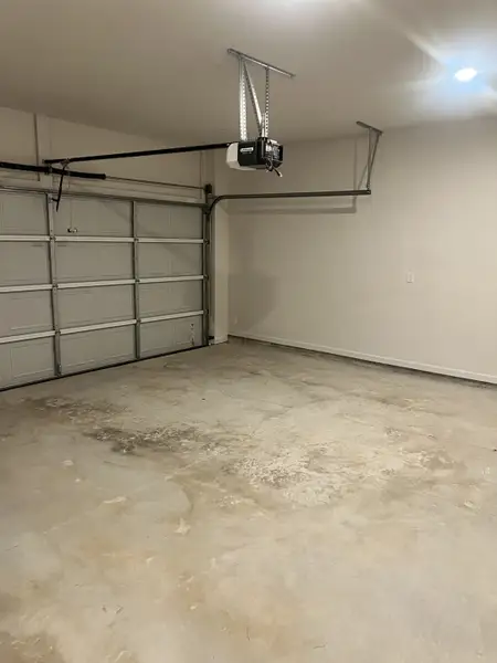 A spacious garage features a smooth concrete floor, an overhead door, and a ceiling-mounted opener for easy access.