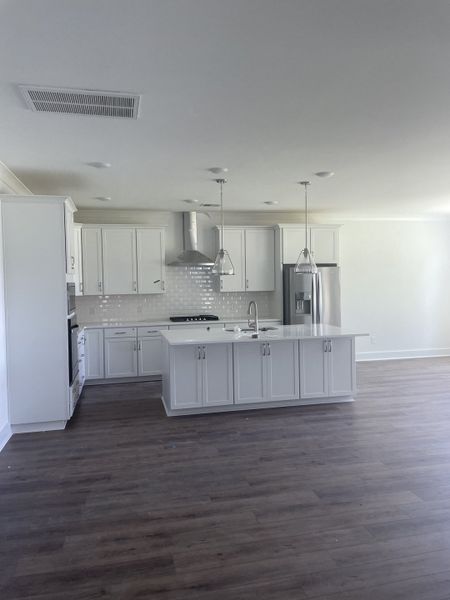 A modern kitchen with white cabinetry, an island, stainless steel appliances, and glass pendant lighting over wood floors.