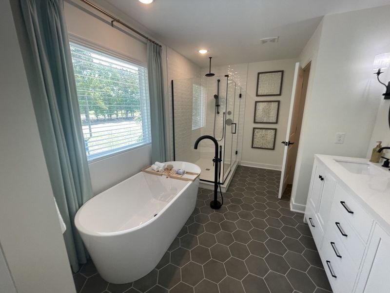 A modern bathroom featuring a freestanding tub, hexagonal tile flooring, and sleek fixtures with ample natural light.