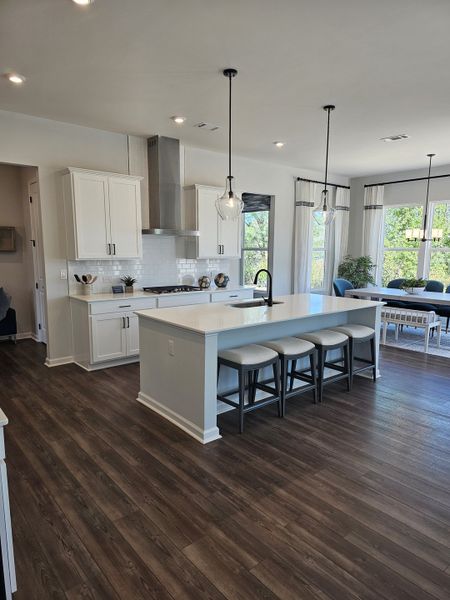 A spacious kitchen with elegant white cabinetry, a large island, modern pendant lights, and dark wood floors.