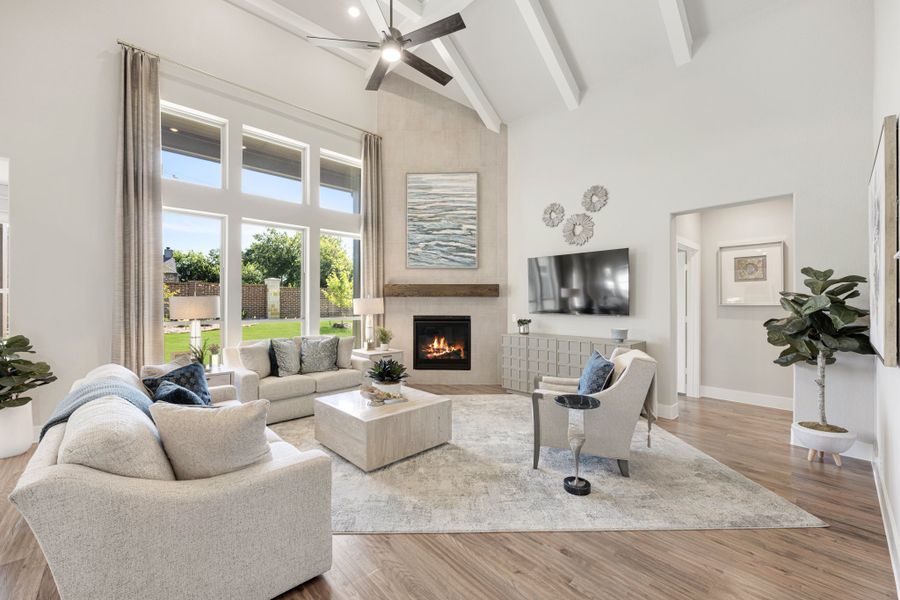 Bright living room with vaulted beamed ceiling, fireplace, hardwood floors, and large windows overlooking backyard