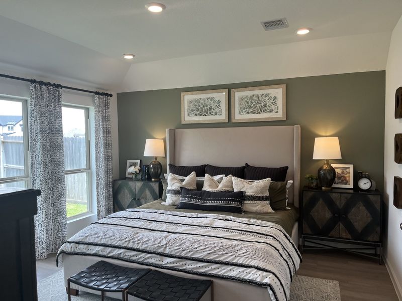 A cozy bedroom with a plush bed, elegant lamps, and stylish decor, featuring green accent wall and natural light.