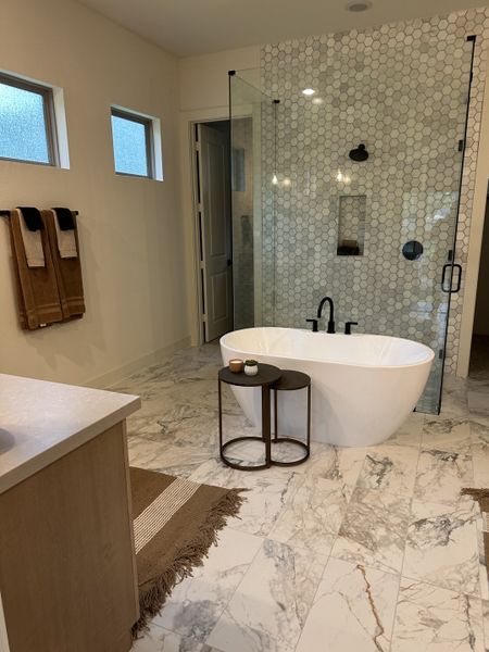 A luxurious bathroom with a freestanding tub, marble floors, hexagonal tile shower, and minimalist decor.
