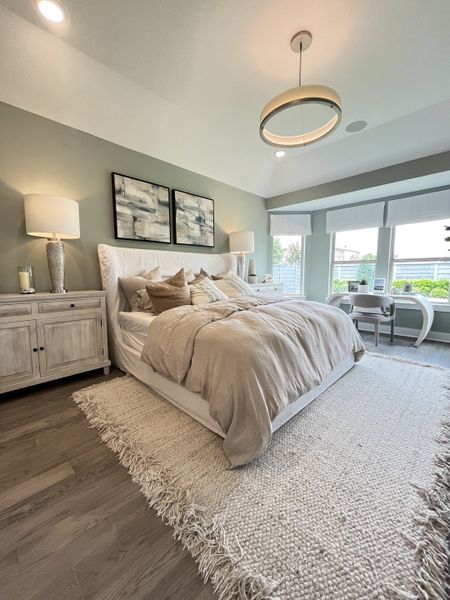 A cozy bedroom with a chic pendant light, soft bedding, and a textured rug, complemented by modern artwork and gentle light tones.