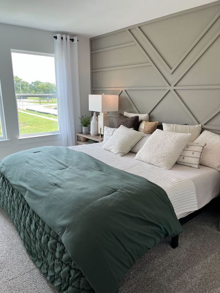 A cozy bedroom with modern geometric wall panels, a soft bed with plush pillows, and a view through large windows.