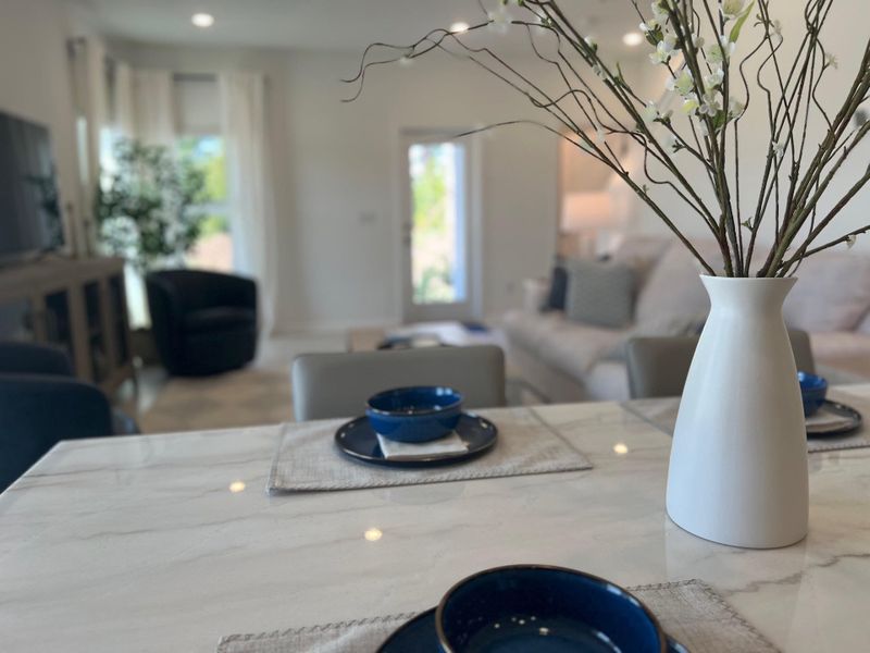 A modern living area with a marble table, elegant vase, and blue dishware, complemented by cozy seating and soft lighting.