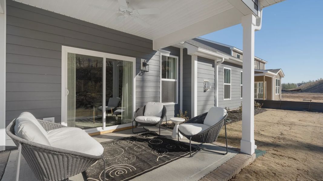 Back of gray exterior sided home with covered porch with sliding door, and ceiling fan at Walnut Ridge by DRB Homes