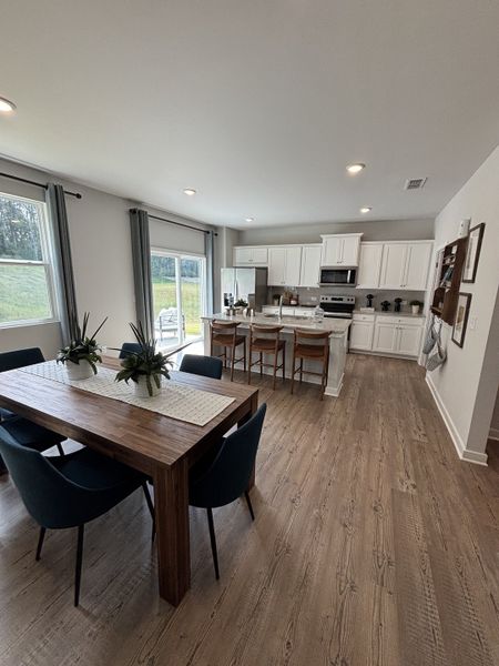 Spacious kitchen with sleek white cabinetry, wooden island seating, and a rustic dining table with modern navy chairs.