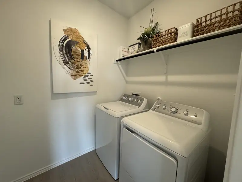 A modern laundry room with sleek white appliances, decorative artwork, and organized shelving for practical storage.