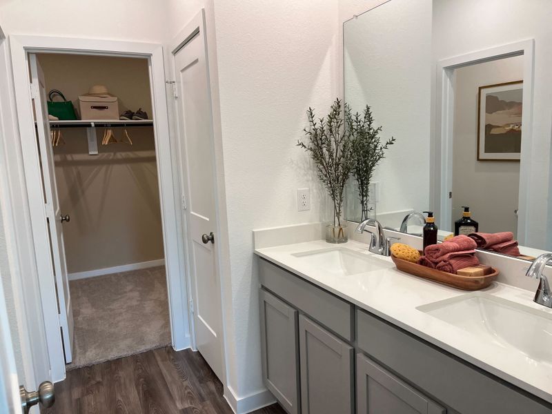 A modern bathroom with dual sinks, elegant cabinetry, and an adjacent walk-in closet. 