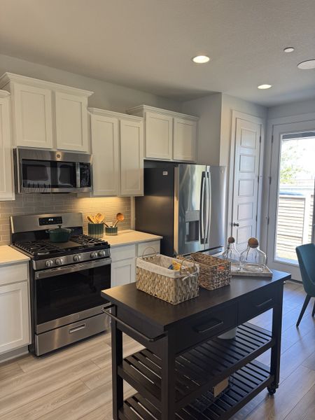 Modern kitchen with sleek white cabinets, stainless steel appliances, and a functional island on wood flooring.