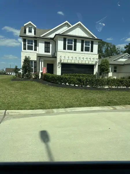 A charming white house with black accents and lush landscaping in Windrow by Centex (Hockley, TX).