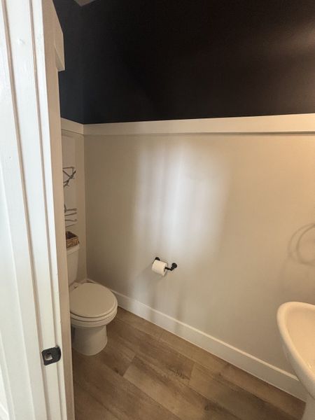 A minimalist half-bath with dark accent walls, wood flooring, and a pedestal sink for a sleek design. A minimalist half-bath with dark accent walls, wood flooring, and a pedestal sink for a sleek design.
