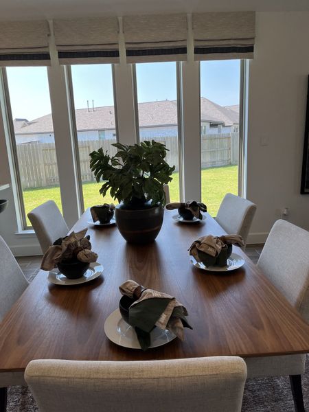 A bright dining area with a sleek wooden table, elegant table settings, and large windows overlooking a lush backyard.