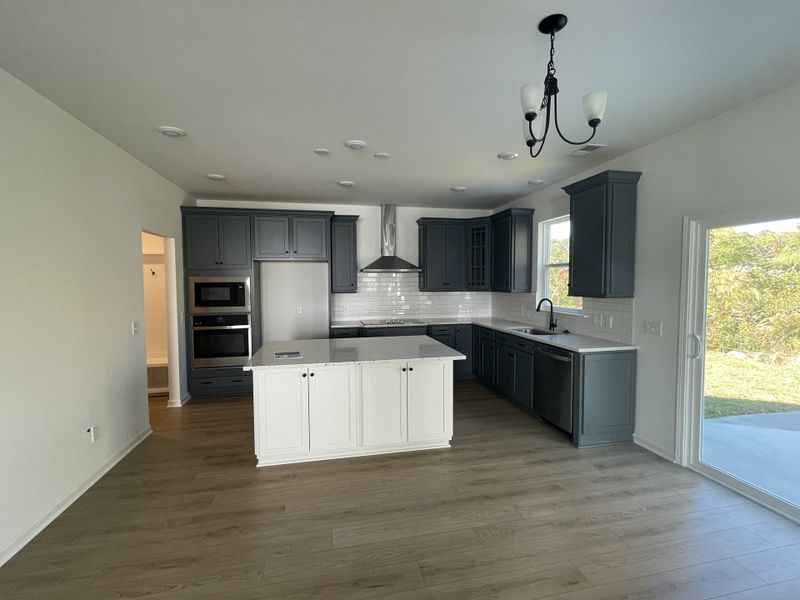 A modern kitchen with dark cabinets, a central island, stainless steel appliances, and sleek lighting.